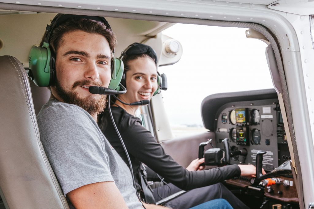 Two students sitting in the cockpit of a plane smiling.