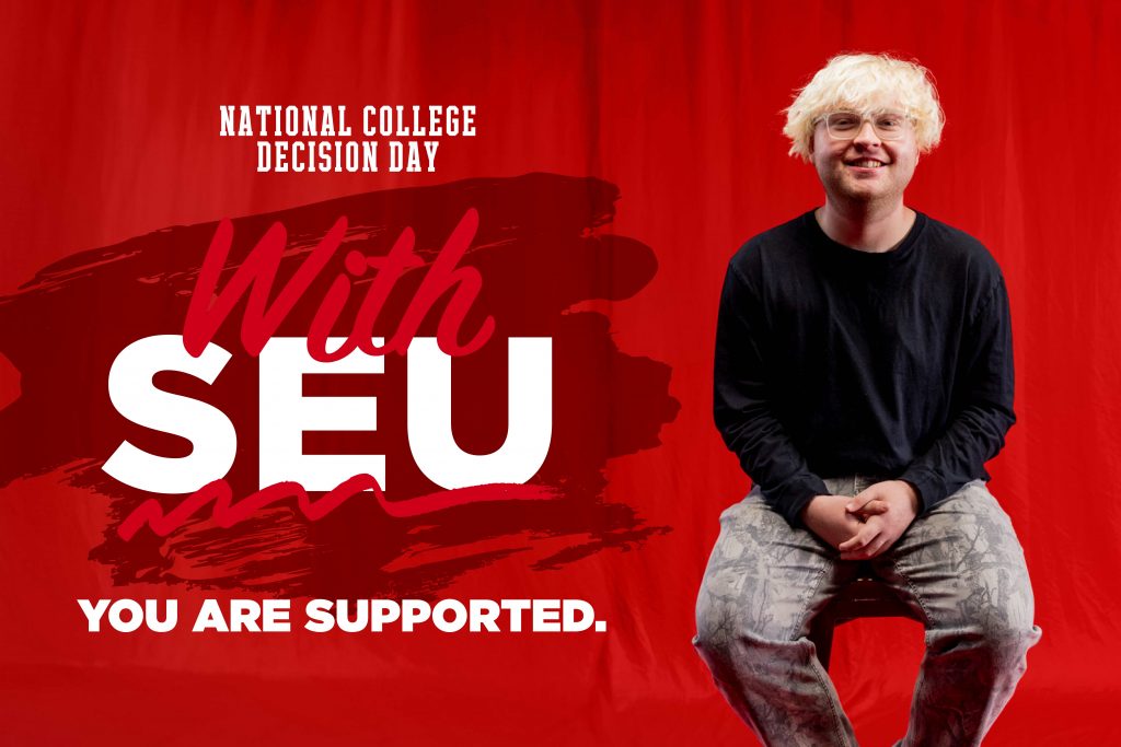 Kohltan, a student at SEU, smiling in front of a read background.