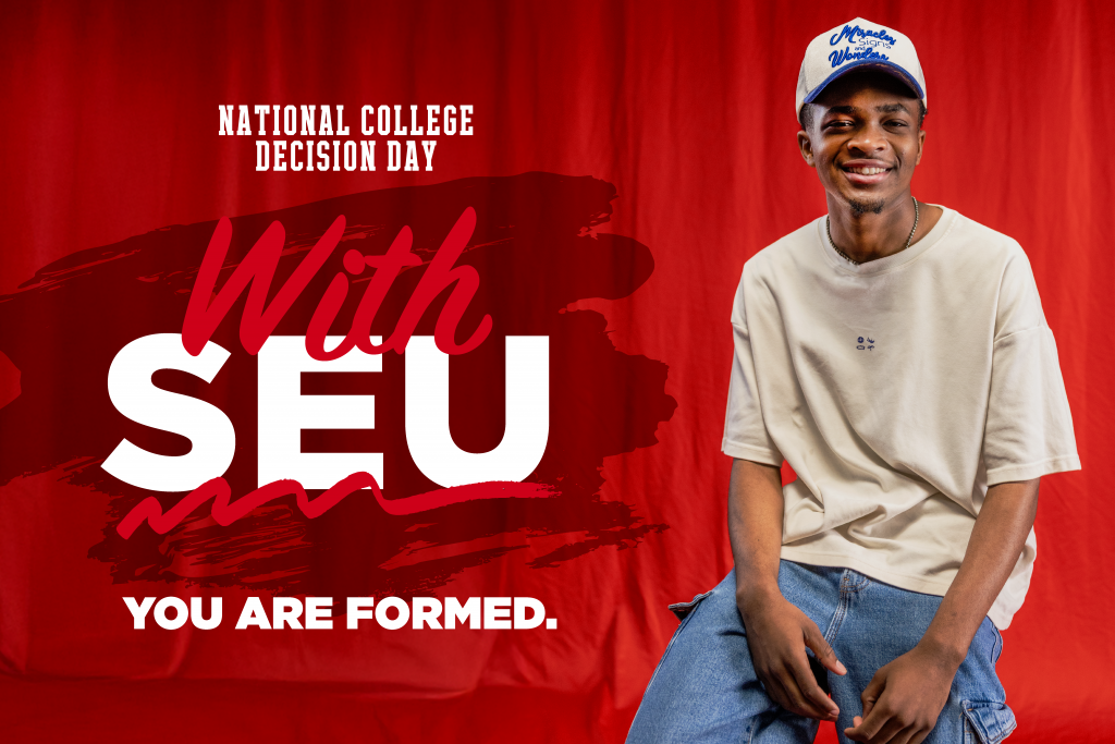 SEU student sitting and smiling in front of a red background