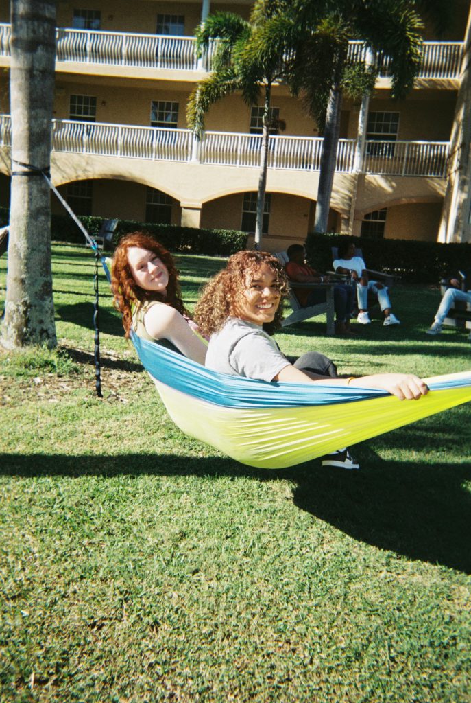 Two students sitting on hammock smiling and laughing