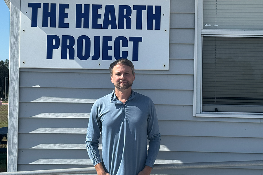 Ben Ruch standing in front of grey building and "The HEARTH Project" sign