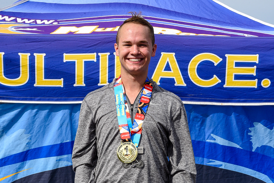 A man wearing a medal is standing in front of a blue sign