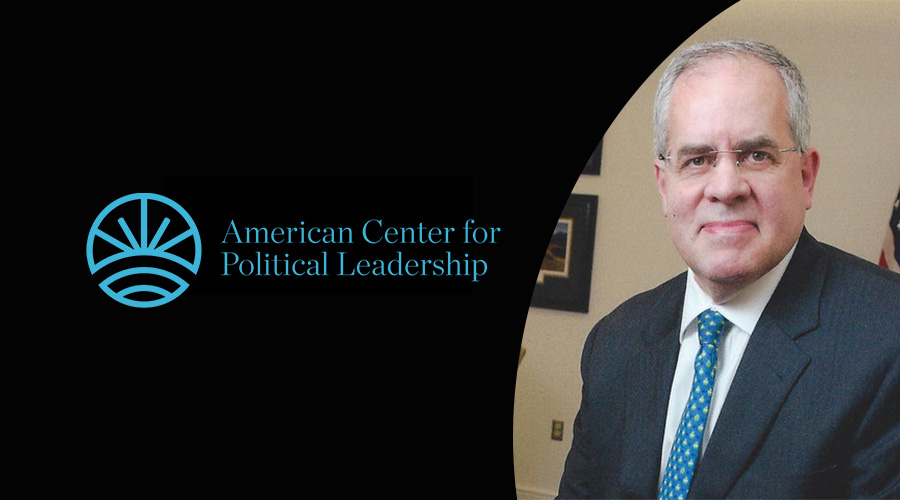 Man smiling in suit while next to American Center for Political Leadership Logo in blue