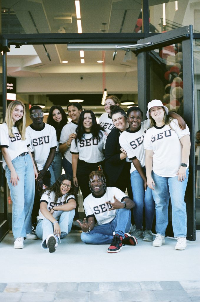 Students are smiling outside the SEU welcome building while wearing white SEU shirts