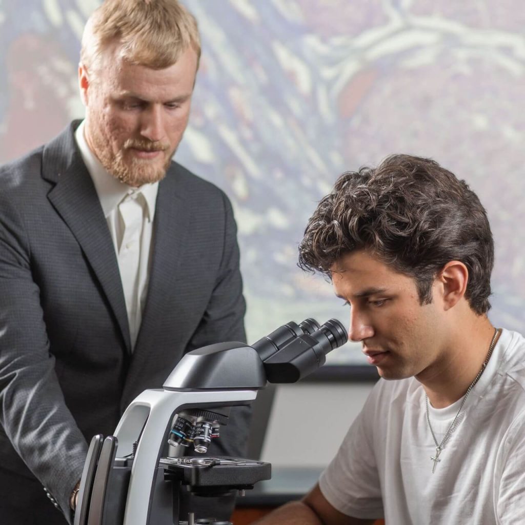 Professor instructing a student on using a microscope