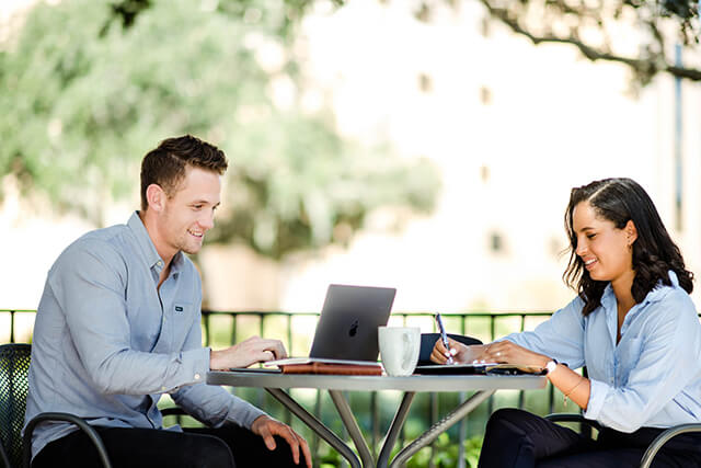 Two individuals working outdoors, immersed in their tasks with laptops, blending productivity with the refreshing ambiance of an outdoor enviorment.