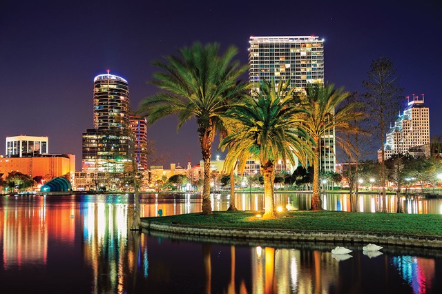 Downtown Orlando at night featuring palm trees and a lighted lakefront trail