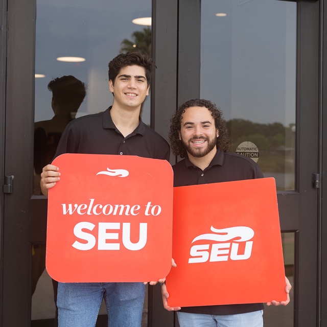 Two male students holding "Welcome to SEU" signs smiling