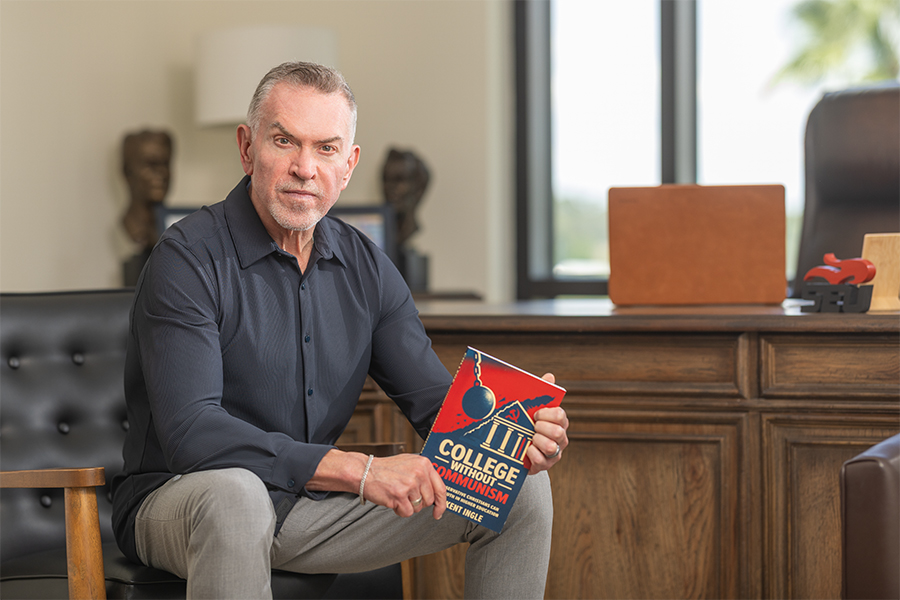 Dr. Kent Ingle sitting in a chair, wearing a blue shirt and holding a copy of his latest book.
