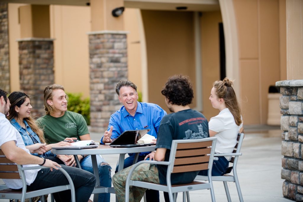 Students sitting around a table with a professor outside