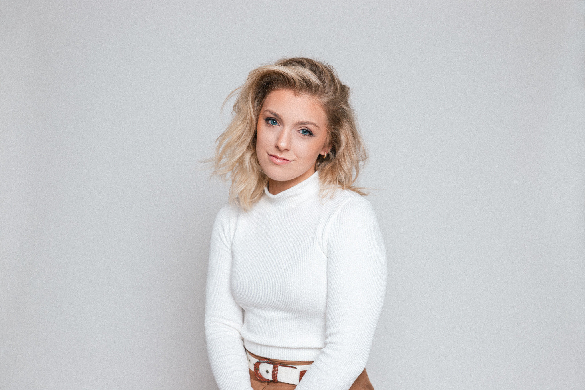 Woman in white long sleeve shirt infront of a grey background.