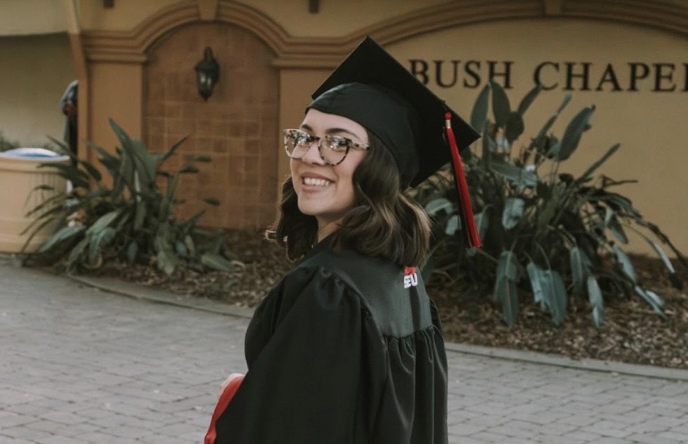 Woman in cap and gown standing in front of Bush Chapel