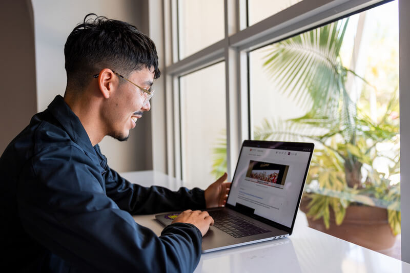 A male student is sitting at a counter using a laptop computer.
