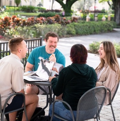 Four students sitting at an outdoor table laughing