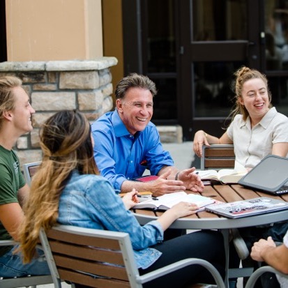 Professor sitting at an outdoor table with a couple of students