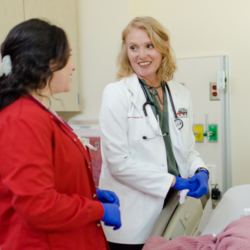 Nursing faculty member Niki Music in white coat smiling at student in red nursing scrubs jacket.