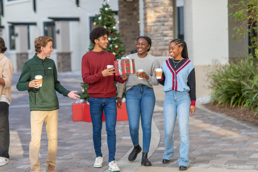 Student's walking while laughing and one of them holding a Christmas present.