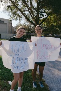 Two young women are holding signs. One sign says Food and Supplies Drive, and the other says Hurricane Relief