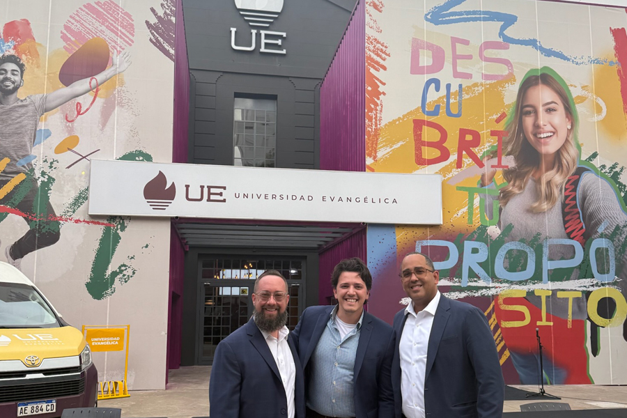 Three men in business suits are standing outside the building of the new Evangelical University in Argentina.