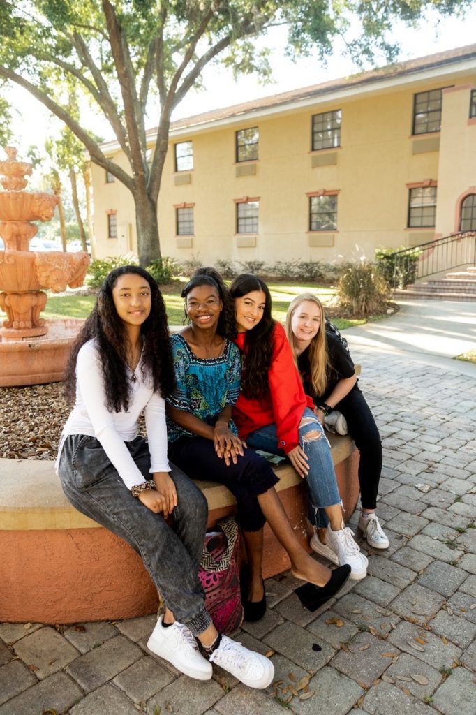 Four female students smiling sitting in front of a fountain on campus