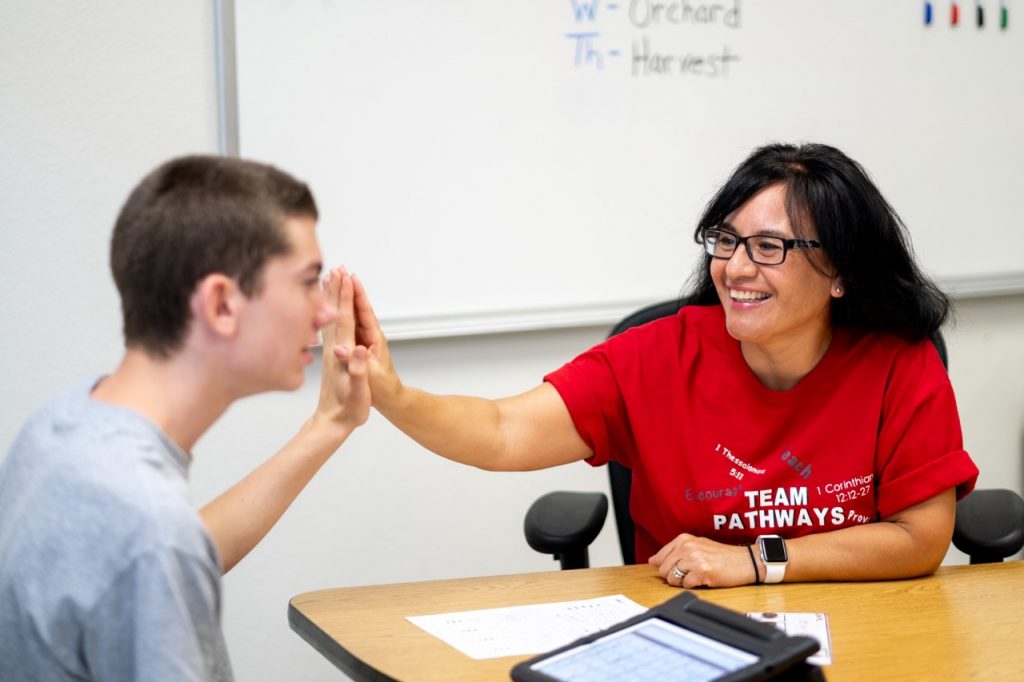 Pathways teacher giving a student a high five sitting at a desk