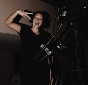 A young woman is smiling as she operates a video camera.