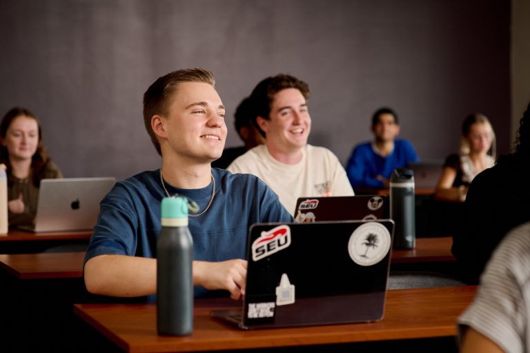 Students sitting at desks with computers smiling