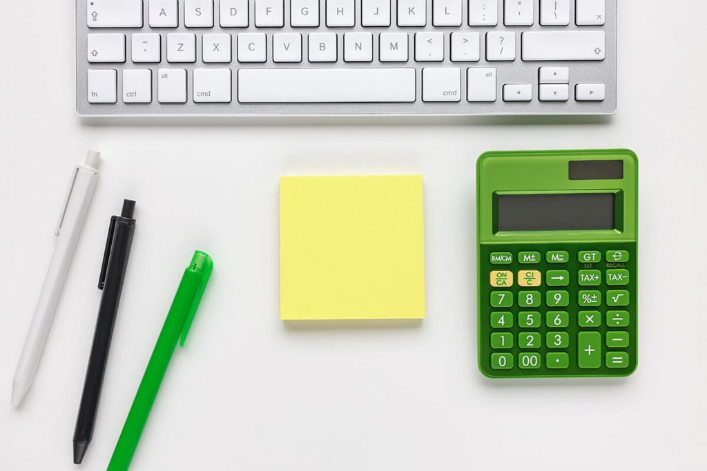 On a desk, a green calculator is positioned alongside a keyboard, accompanied by neatly arranged note taking materials.