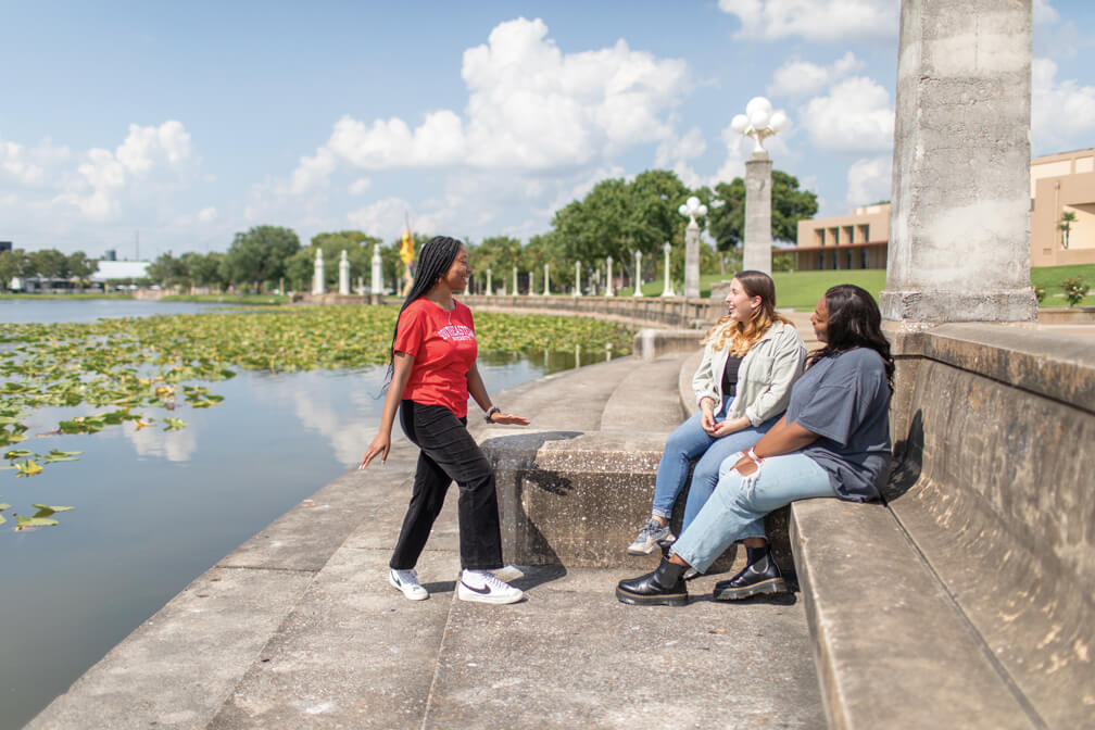 Students laughing and smiling while wearing red SEU t-shirt next to lake