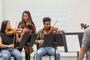 Professor watching students practice violin in class.