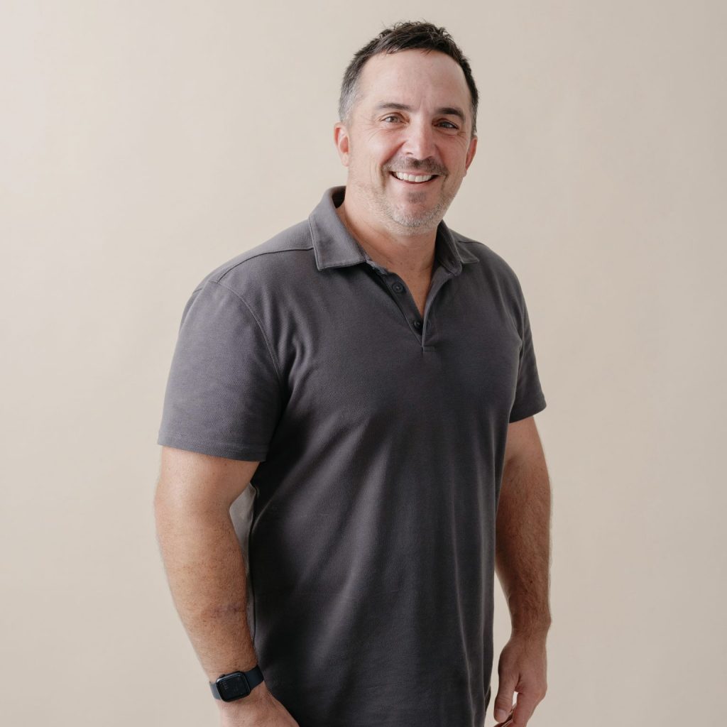 Midshot of a man in front of a gray background.